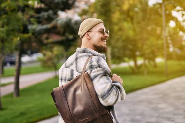 Sakallı mutlu hippi öğrencinin şehir parkında yürürken kahve içmesi. Dinlenme günü 