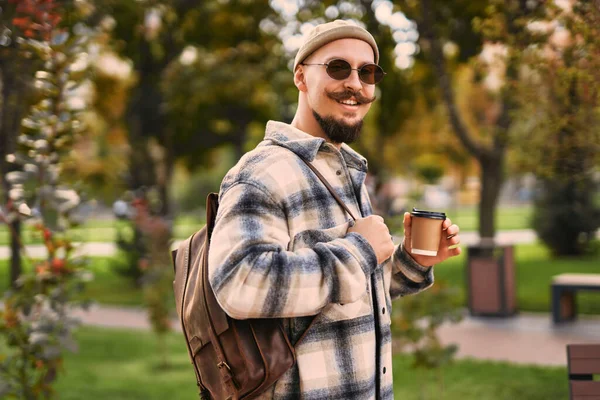 Half length of happy face of guy walk around park outdoor holds coffee to go while having relax time