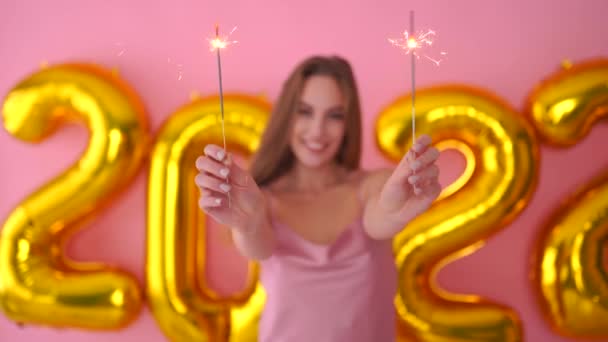 Kvinna hålla tomtebloss och ett glas champagne, poserar med 2022 nyår ballonger på rosa bakgrund — Stockvideo
