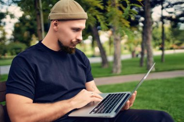 Ciddi bir serbest çalışan dışarıda oturup dizüstü bilgisayarla yazı yazıyor. 5G internet bağlantısı