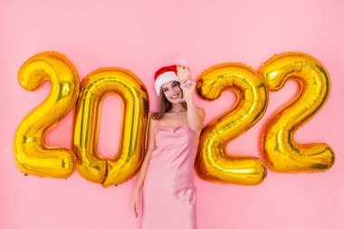 Heyecanlı kız Noel Baba şapkasıyla şampanya kadehini kaldırıyor. 2022 Altın Hava Balonları Yeni Yıl Konsepti 