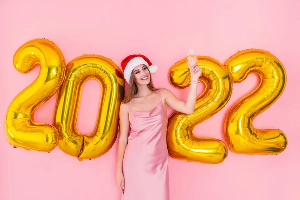 A jovem Santa excitada levanta uma taça de champanhe. Números dourados balões de ar conceito de Ano Novo — Fotografia de Stock