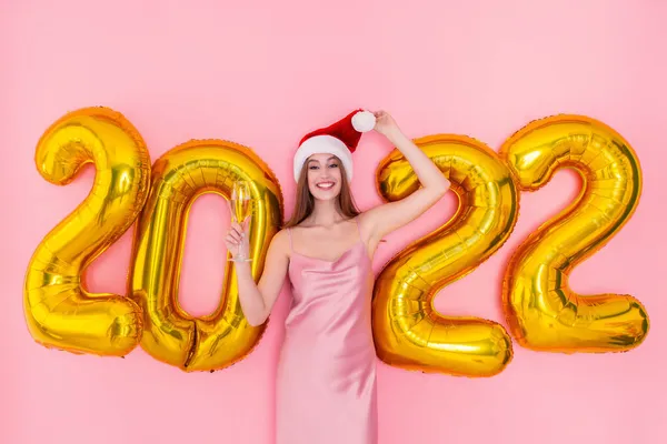Mulher sorridente segura copo de champanhe em chapéu Santas 2022 balões de ar dourado conceito de Ano Novo — Fotografia de Stock