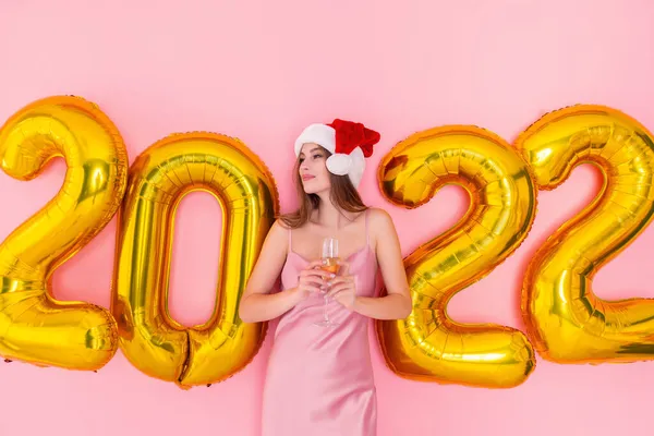 Mulher excitada segura copo de champanhe no chapéu Santas olha para o lado. balões de ar dourado 2022 Ano Novo — Fotografia de Stock