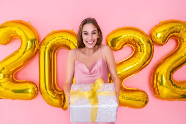 Heyecanlı kadın hediye kutusunu pembe arka planda 2022 hava balonunda izole halde tutuyor. Yeni yıl kutlaması 