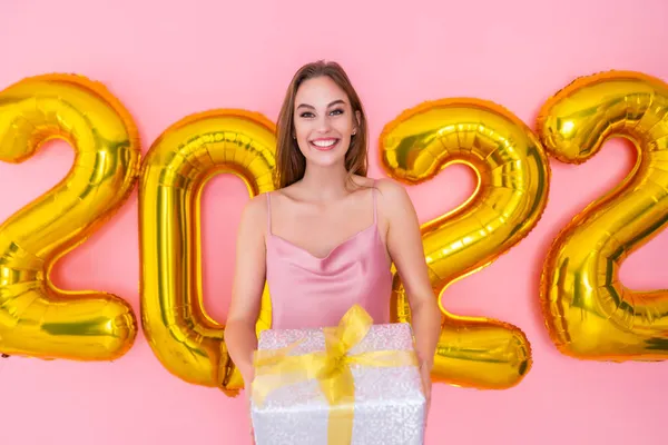 Lächelnde Frau hält Geschenkbox isoliert auf rosa Hintergrund 2022 Luftballons. Neujahrsfeier — Stockfoto