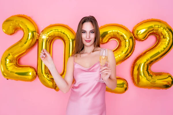 Половина улыбающейся девушки держит в руках искру и шампанское. Воздушные шары 2022 года — стоковое фото