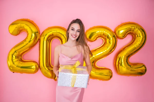 Glückliches Mädchen hält Geschenk-Box isoliert auf rosa Hintergrund 2022 Luftballons. Neujahrsfeier — Stockfoto