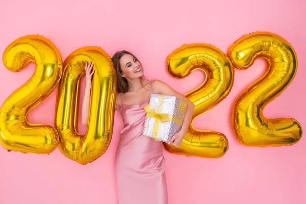 Glückliche Frau steht neben Luftballons mit Geschenkschachteln auf rosa Hintergrund. Neujahrsfeier — Stockfoto
