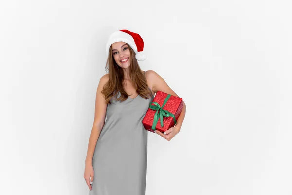Mujer caucásica feliz en el sombrero de Santas sostiene presente mientras que está parado sobre fondo blanco. Celebración — Foto de Stock