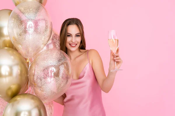 La mitad de la longitud de la muchacha feliz levanta la copa del champán se para cerca de los globos dorados aéreos. Celebración — Foto de Stock