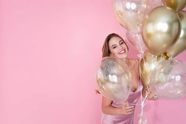 Chica alegre sostiene muchos globos aéreos dorados sobre fondo rosa. cumpleaños, fiesta de año nuevo —  Fotos de Stock