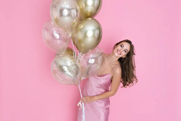 Chica feliz sostiene muchos globos aéreos dorados sobre fondo rosa. cumpleaños, fiesta de año nuevo —  Fotos de Stock