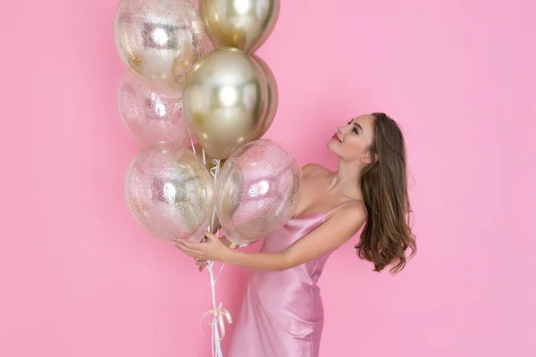 Nettes erwachsenes Mädchen hält viele goldene Luftballons auf rosa Hintergrund. Geburtstag, Neujahrsfeier — Stockfoto
