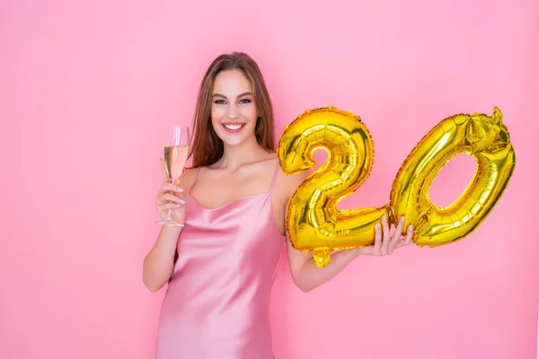 Die junge glückliche Frau hält einen Luftballon mit Goldfolie und ein Glas Champagner auf rosa Hintergrund. GEBURTSTAGPARTY — Stockfoto