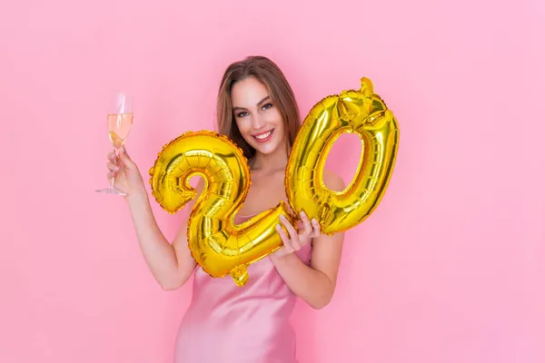 Junge lächelnde Frau hält Luftballon mit Goldfolie und ein Glas Champagner auf rosa Hintergrund BIRTHDAY PARTY — Stockfoto