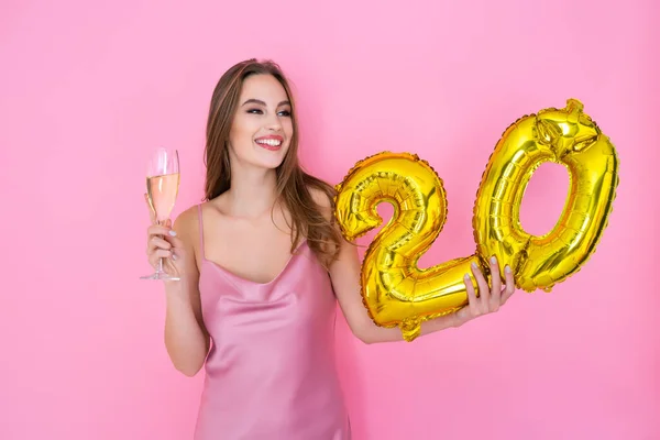 Das junge glückliche Mädchen hält einen Ballon mit Goldfolie und ein Glas Champagner auf rosa Hintergrund. GEBURTSTAGPARTY — Stockfoto