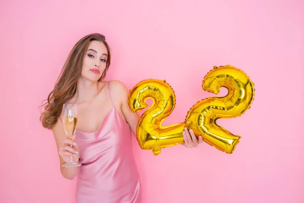 Junge lächelnde Frau hält Luftballon mit Goldfolie und ein Glas Champagner auf rosa Hintergrund BIRTHDAY PARTY — Stockfoto