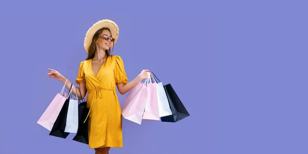 Vacker kvinna i solglasögon och hatt håller färgglada shoppingväskor på lila bakgrund. Försäljningsidé — Stockfoto