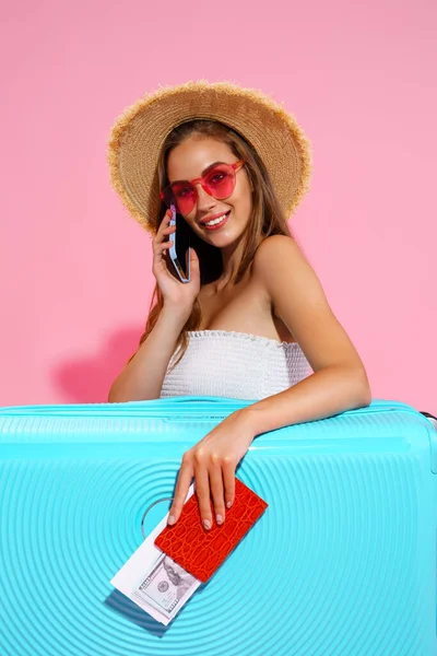 Щаслива дівчина в літньому одязі з багажем тримає квиток, паспорт, гроші під час розмови по телефону — стокове фото