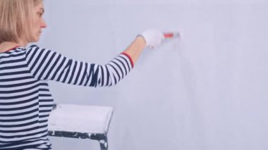 Sarışın kadının arka görünüşü duvarı beyaz bir fırçayla boyuyor. yenileme konsepti