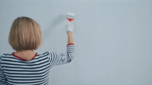 Rückansicht der blonden Frau bemalt die Wand mit einem Pinsel mit weißer Farbe. Sanierungskonzept — Stockvideo