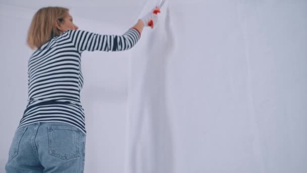 Die Rückansicht einer Frau bemalt die Wand in weißer Farbe, während sie auf der Treppe steht. Sanierungskonzept — Stockvideo