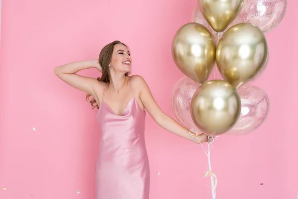 Emotionales Mädchen hält viele goldene Luftballons auf rosa Hintergrund. Geburtstag, Neujahrsfeier — Stockfoto