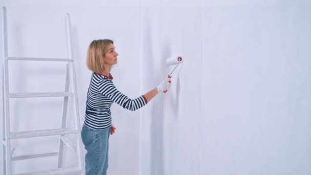 Vista laterale di donna concentrata pittura con rullo intonacato parete in colore bianco — Video Stock
