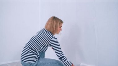 Duvarı fırça silindiriyle boyayan genç sarışın kadın. Yeni konut ve DIY yenileme kavramı.