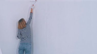 Duvarı fırça rulosuyla boyayan beyaz bir kadın. Yeni konut ve DIY yenileme kavramı.