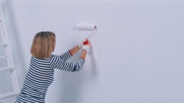 Duvarı fırça silindiriyle boyayan genç bir kadın. Yeni konut ve DIY yenileme kavramı.