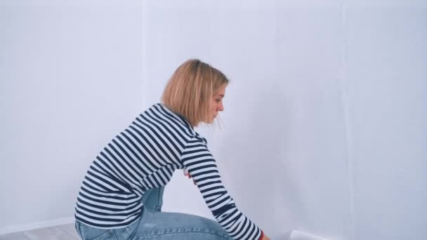 Νεαρή ξανθιά γυναίκα βάφει τον τοίχο με ρολό πινέλου. Νέα έννοια στέγασης και ανακαίνισης DIY. — Αρχείο Βίντεο
