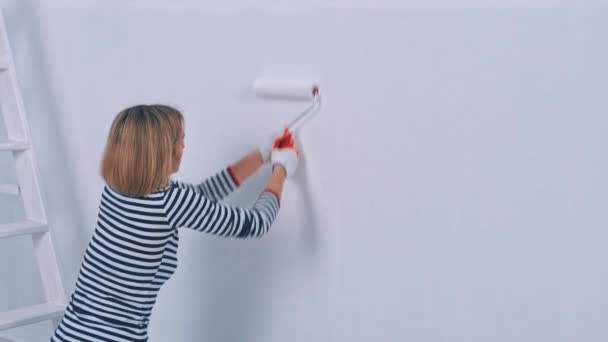 Duvarı fırça silindiriyle boyayan genç bir kadın. Yeni konut ve DIY yenileme kavramı. — Stok video
