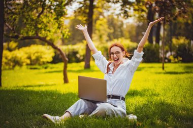 Neşeli duygusal kızın portresi parkta otururken dizüstü bilgisayarı açık havada eğleniyor.