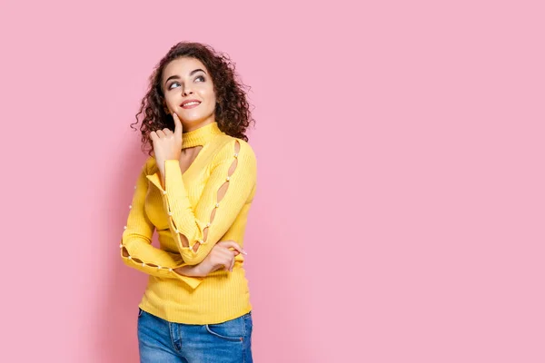 Menina encaracolado bonito pensivo em roupa amarela colocar adereço de mão no queixo isolado no fundo rosa — Fotografia de Stock