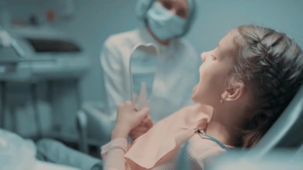 Paciente infantil e dentista feminina verificando os dentes no espelho após o tratamento odontológico no consultório odontológico — Vídeo de Stock