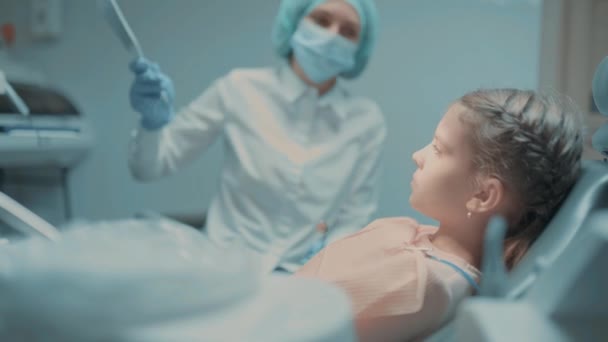 Kleine Patientin und Zahnärztin prüfen nach Zahnbehandlung in Zahnarztpraxis Zähne am Spiegel — Stockvideo