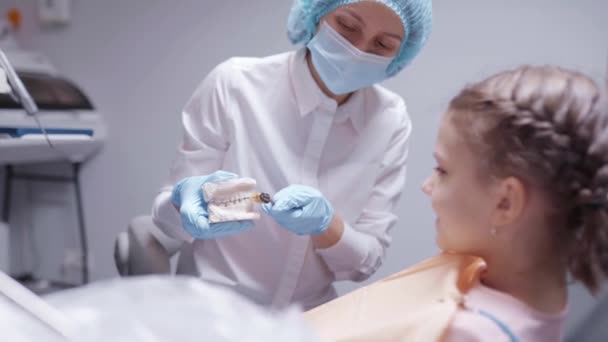 Dentista amigável educa menina para escovar os dentes corretamente usando modelo dental. conceito de odontologia — Vídeo de Stock