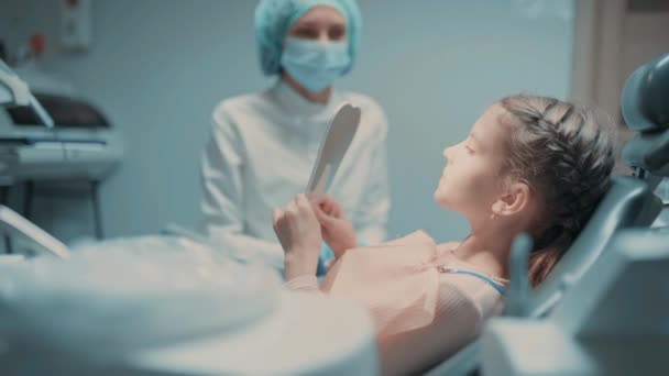 Pequeño paciente y dentista están revisando los dientes en el espejo. Niño gestos pulgares hacia arriba y sonriendo — Vídeos de Stock