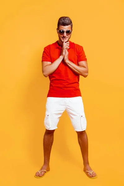 Longitud completa del hombre hipster en camiseta roja y pantalones cortos blancos en gafas de sol se levanta sobre fondo amarillo — Foto de Stock
