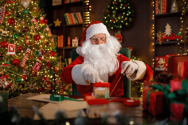 Der Weihnachtsmann bereitet Geschenke für Kinder zu Weihnachten vor, während er zu Hause am Schreibtisch sitzt. Neues Jahr — Stockfoto