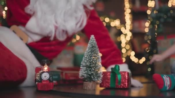 幼い男の子がサンタクロースと電車でクリスマスツリーの下で遊んでいるビデオ. — ストック動画