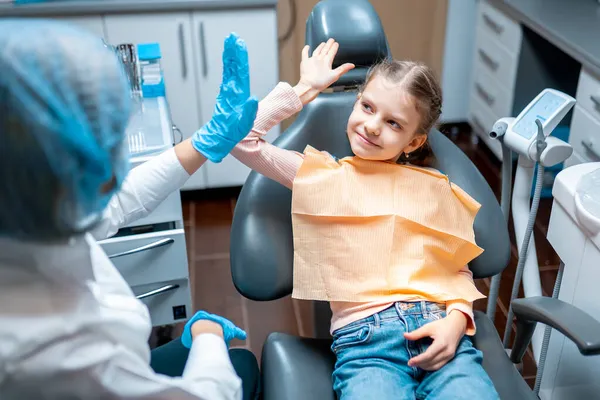 Dost canlısı dişçi muayeneden sonra dişçi koltuğunda oturan beş küçük kız hastaya beşlik çakıyor. — Stok fotoğraf