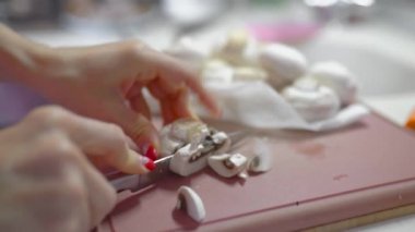 Kesme tahtasına yakın plan doğranmış şampiyon mantarları. Kadınların elleri mantar kesiyor. Beyaz genç kadın aşçı.