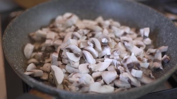 As partes de cogumelos fritam-se em uma panela. Champinhons fatiados, fritos em óleo — Vídeo de Stock