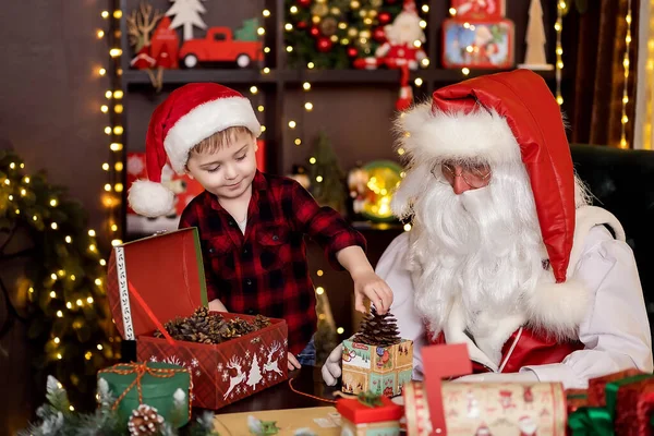 Санта-Клаус с маленьким помощником мальчика упаковки рождественские подарки для детей. НОВОГОДОВОЙ КОНЦЕПТ — стоковое фото
