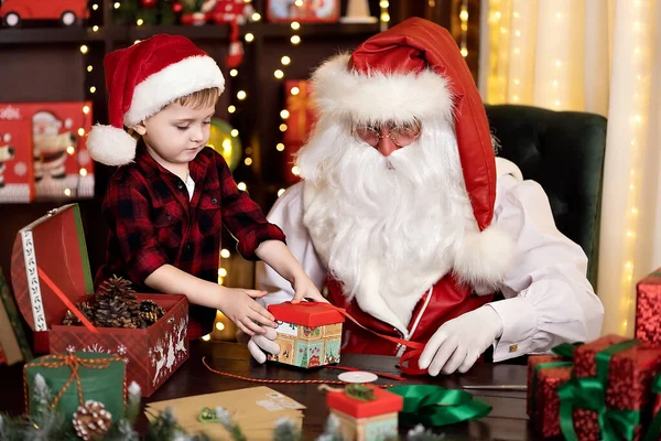Санта Клаус з маленьким хлопчиком-асистентом збирає подарунки для дітей. НОВИЙ РІК ЗБОРІВ — стокове фото
