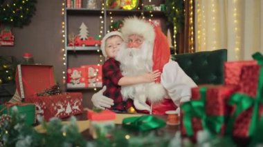 Küçük çocuk Noel Baba 'ya sarılıyor. Çocuk büyülü büyükbabasıyla tanıştığı için mutlu. Çocuk için mutlu bayramlar. 
