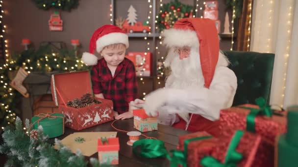 Babbo Natale e piccolo assistente imballare i regali di Natale per i bambini. NUOVO ANNO DI NATALE CONCEPT — Video Stock